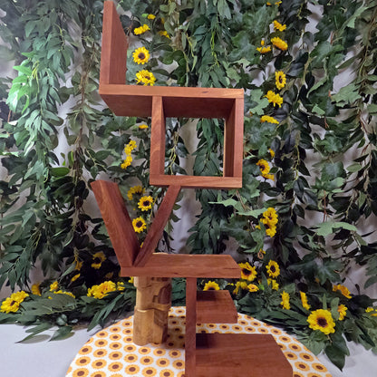 Wooden sculpture with geometric design against a green leafy background
