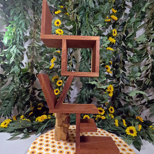 Wooden sculpture with geometric design against a green leafy background