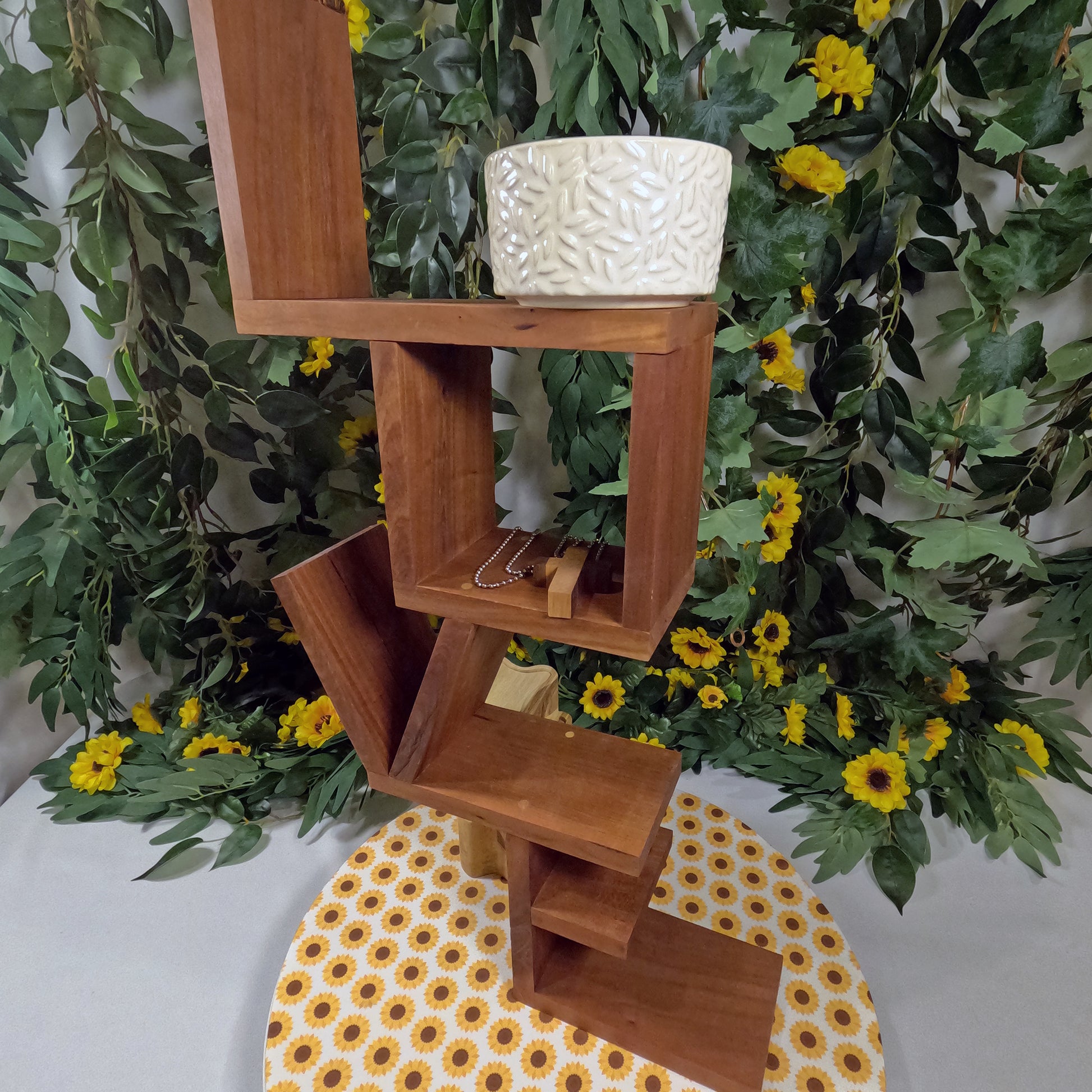 Wooden shelf with a textured white pot against a green leafy background with yellow flowers.