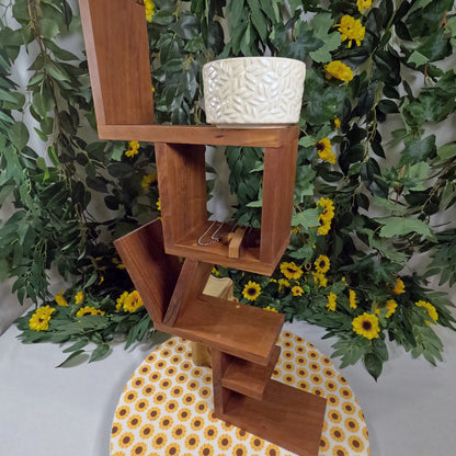 Wooden shelf with a textured white pot against a green leafy background with yellow flowers.