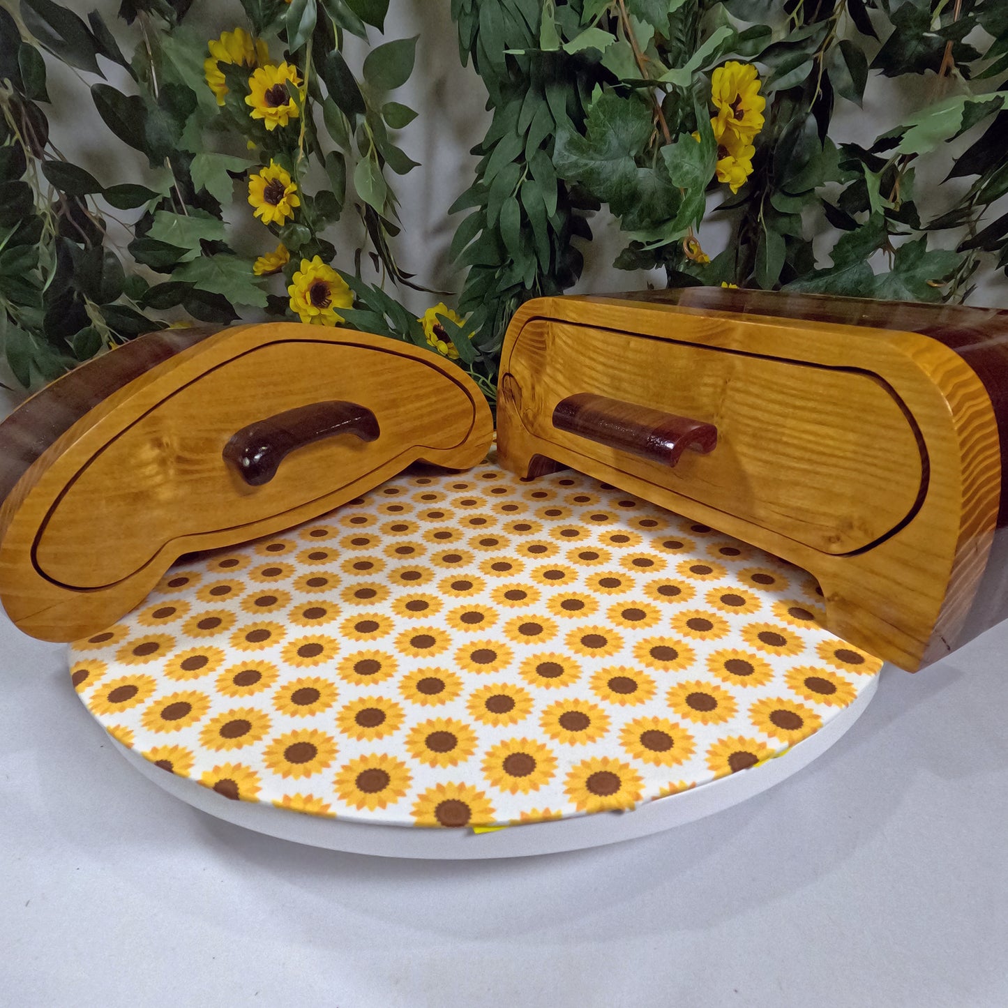Wooden jewelry boxes with a sunflower patterned lid on a white surface with greenery and flowers in the background.