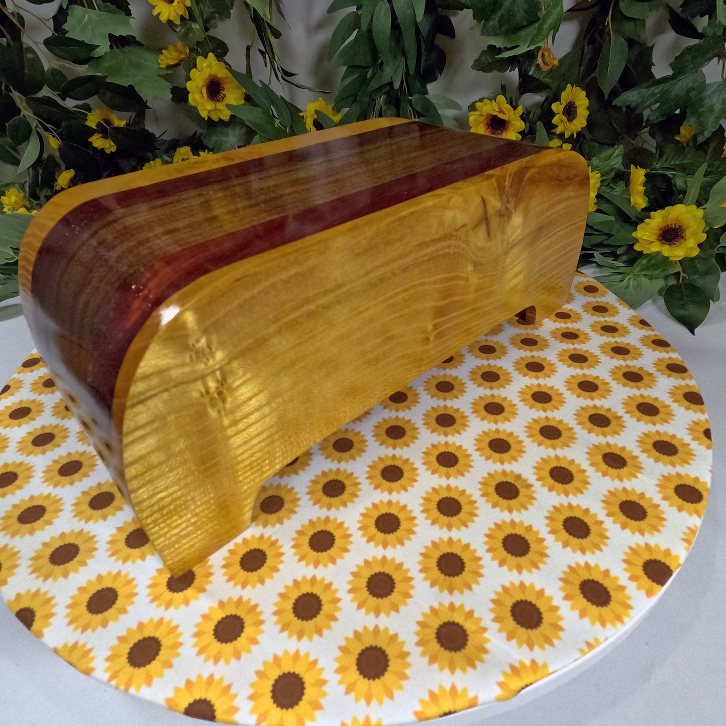 Wooden box on a tablecloth with sunflower pattern, surrounded by greenery and flowers.
