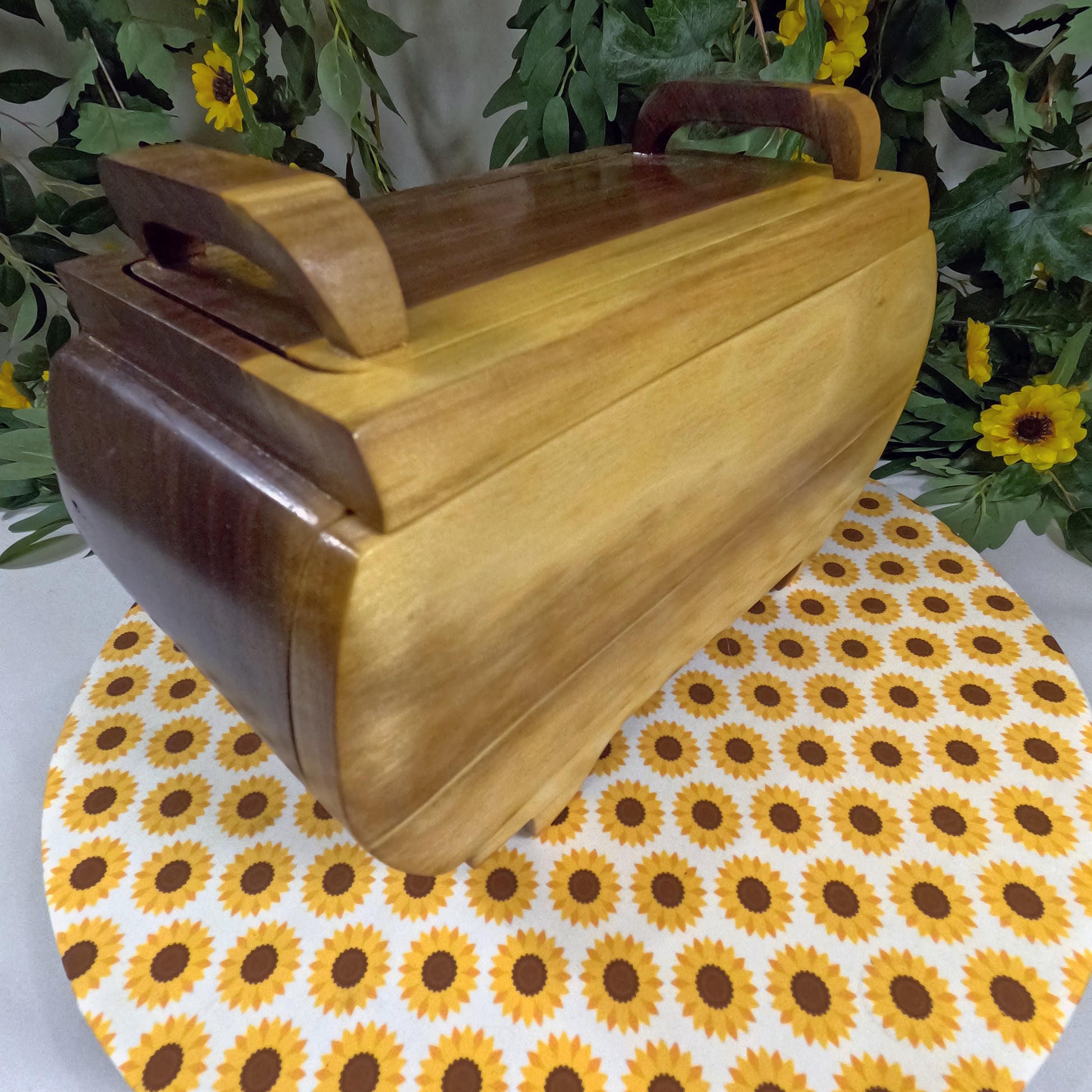 Wooden jewelry box on a sunflower-patterned mat with greenery in the background
