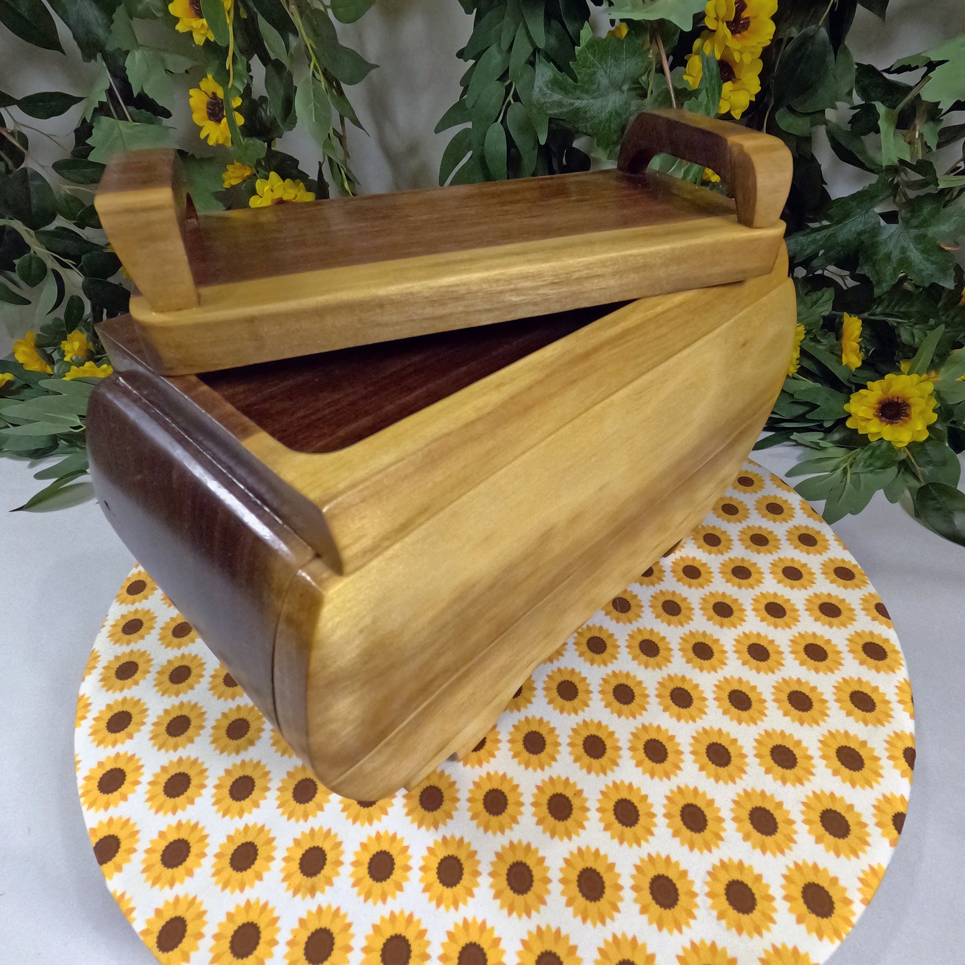 Wooden box with a handle on a sunflower-patterned surface with greenery in the background