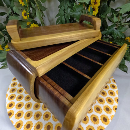 Wooden jewelry box with open lid on a sunflower-patterned surface with greenery in the background