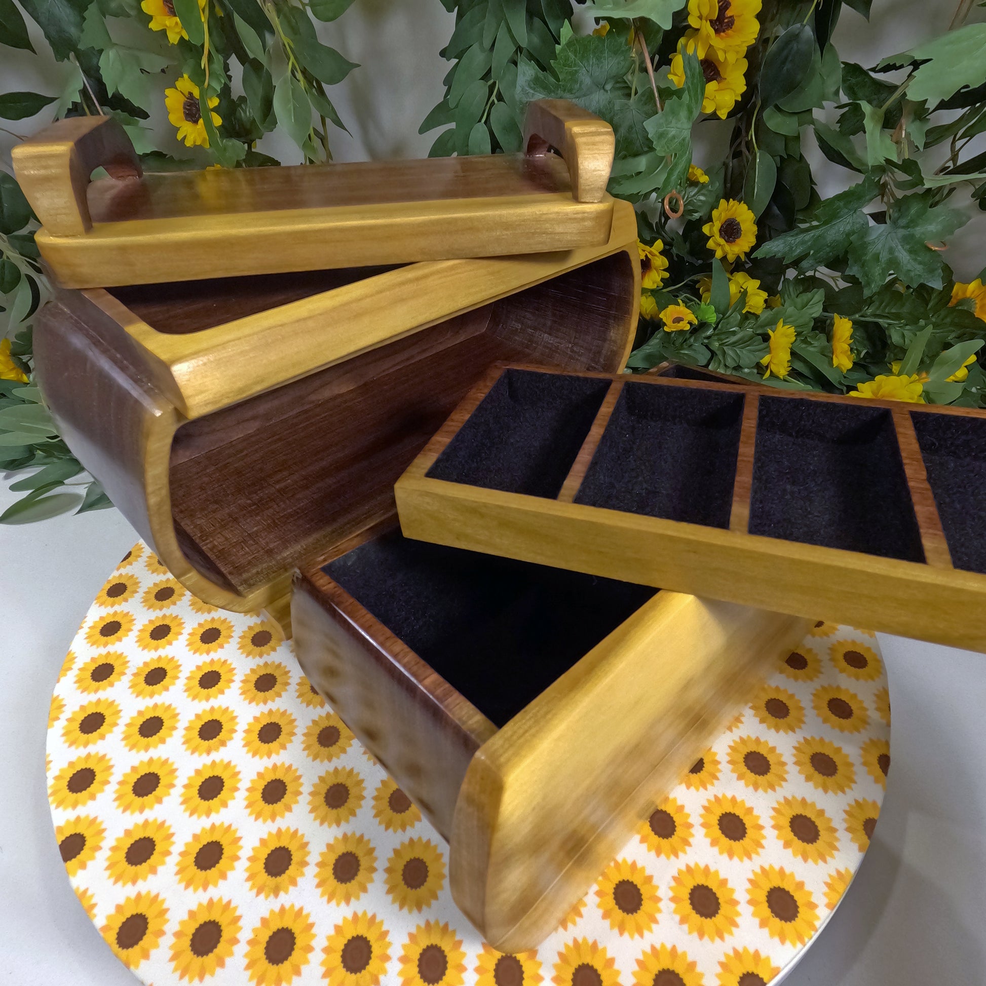 Wooden jewelry box with open lid on a sunflower-patterned surface with greenery in the background