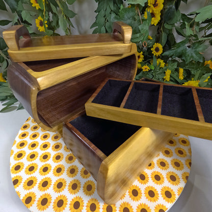 Wooden jewelry box with open lid on a sunflower-patterned surface with greenery in the background