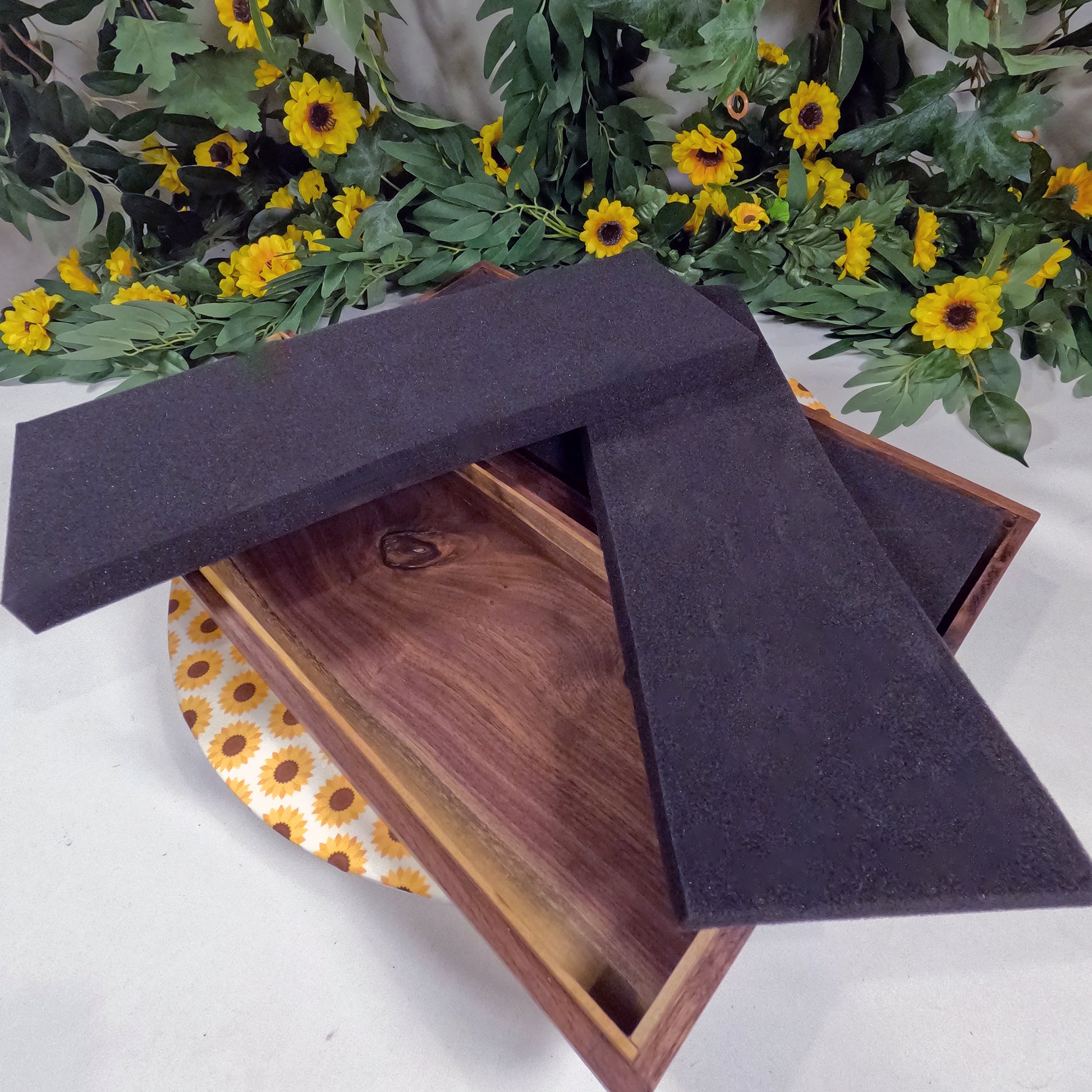 Wooden box with black foam pads on a white surface with floral decorations.