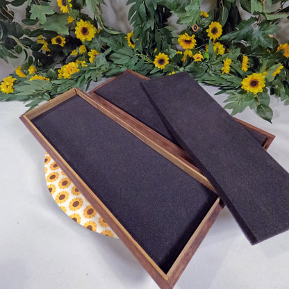 Wooden box with dark interior on a white surface with yellow flowers and green leaves in the background