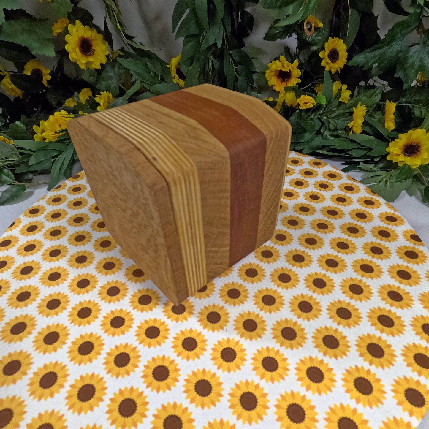 Wooden block on a tablecloth with sunflower pattern, surrounded by greenery and sunflowers.