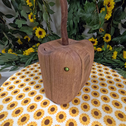 Wooden apple with a handle on a tablecloth with sunflower pattern, surrounded by greenery and flowers.