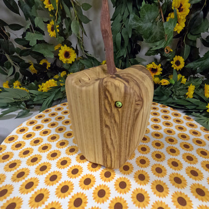 Wooden apple with a handle on a tablecloth with sunflower pattern, surrounded by greenery and yellow flowers.