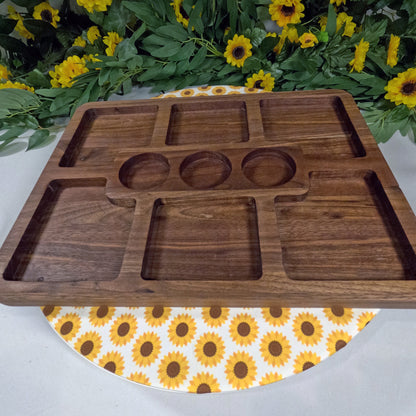 Wooden tray with geometric cutouts on a white surface with sunflower pattern, surrounded by greenery and sunflowers.