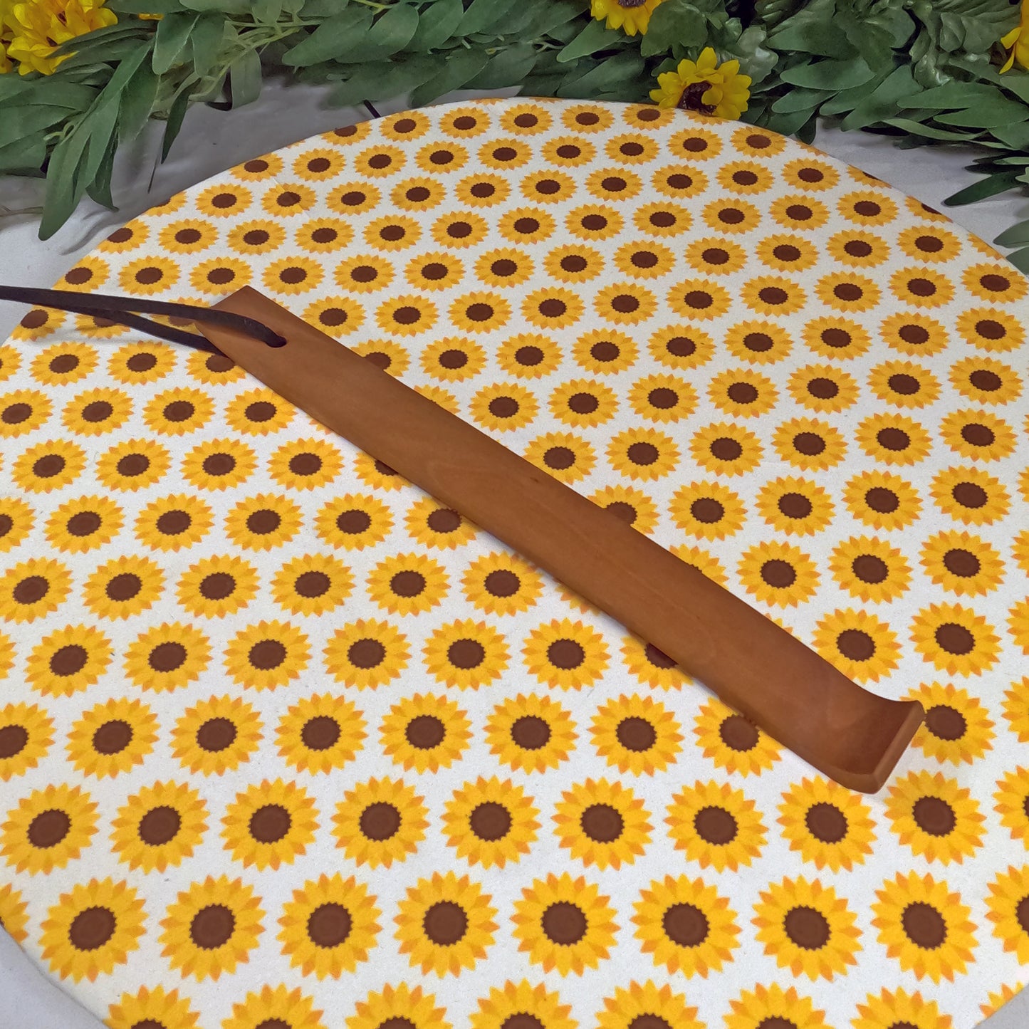 Wooden back scratcher on a sunflower-patterned mat with greenery around.