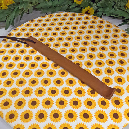Wooden back scratcher on a sunflower-patterned mat with greenery around.