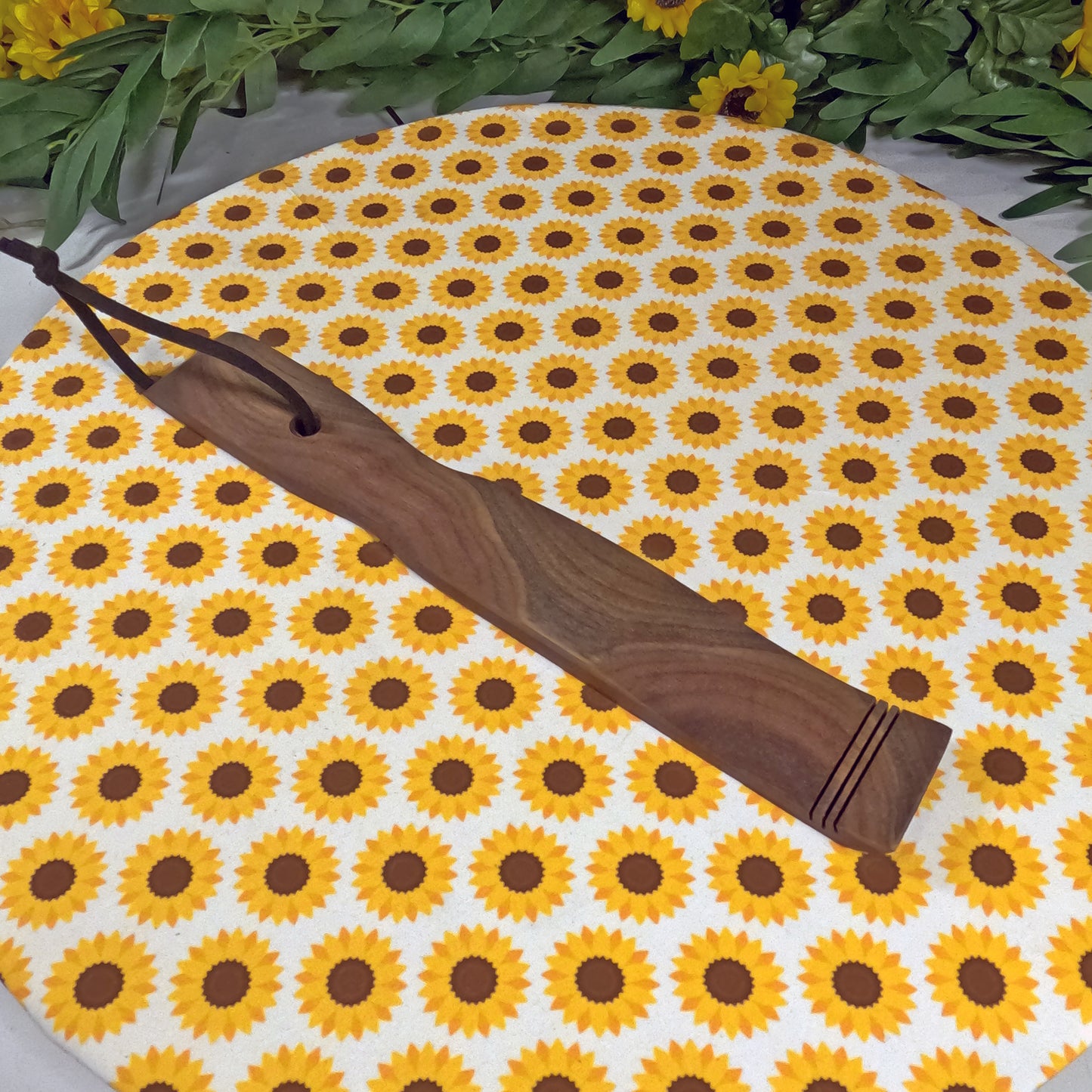 Wooden back scratcher  on a sunflower-patterned mat with greenery around