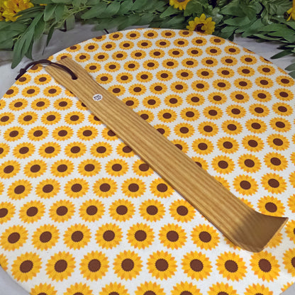 Wooden back scratcher  on a sunflower-patterned mat with greenery in the background