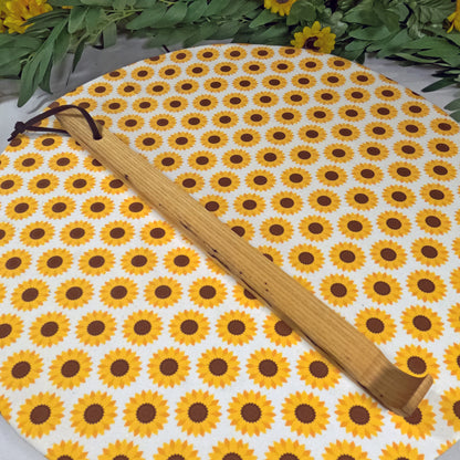 Wooden back scratcher  on a sunflower-patterned mat with greenery around.