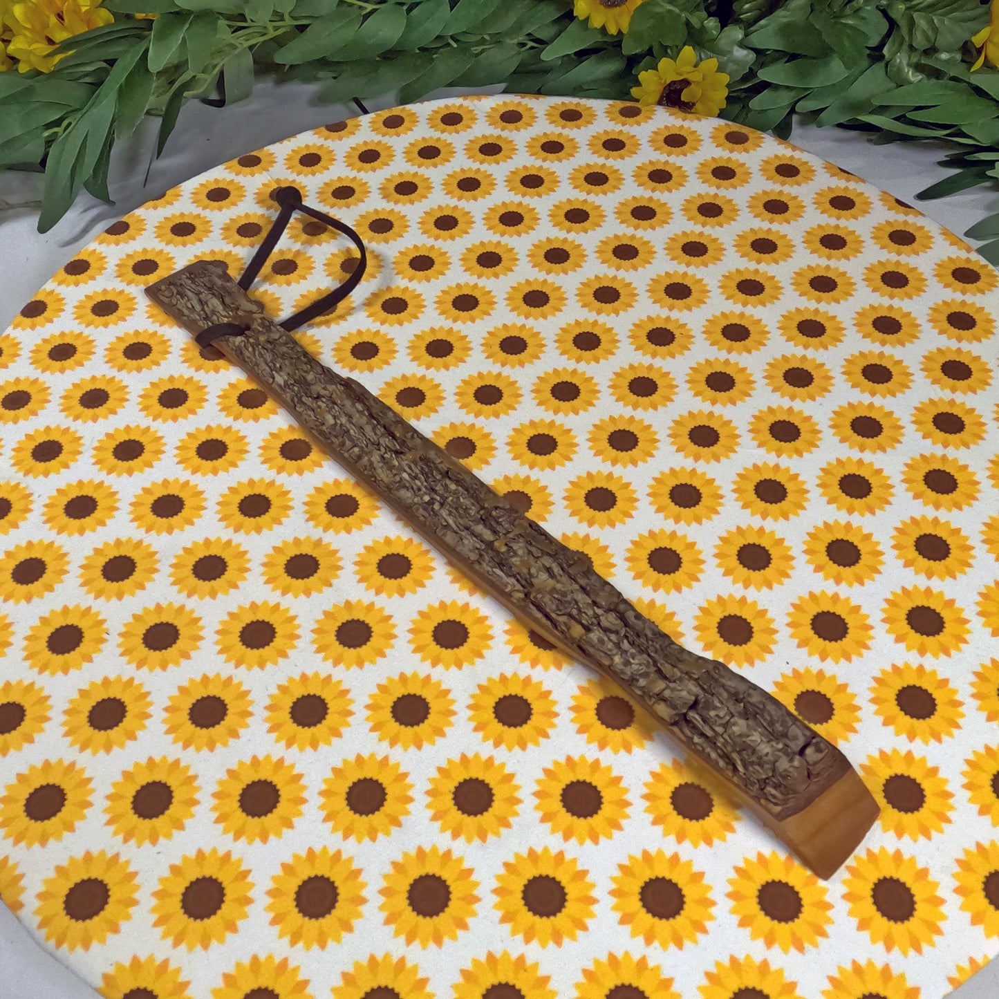 Wooden back scratcher  on a sunflower patterned mat with greenery around