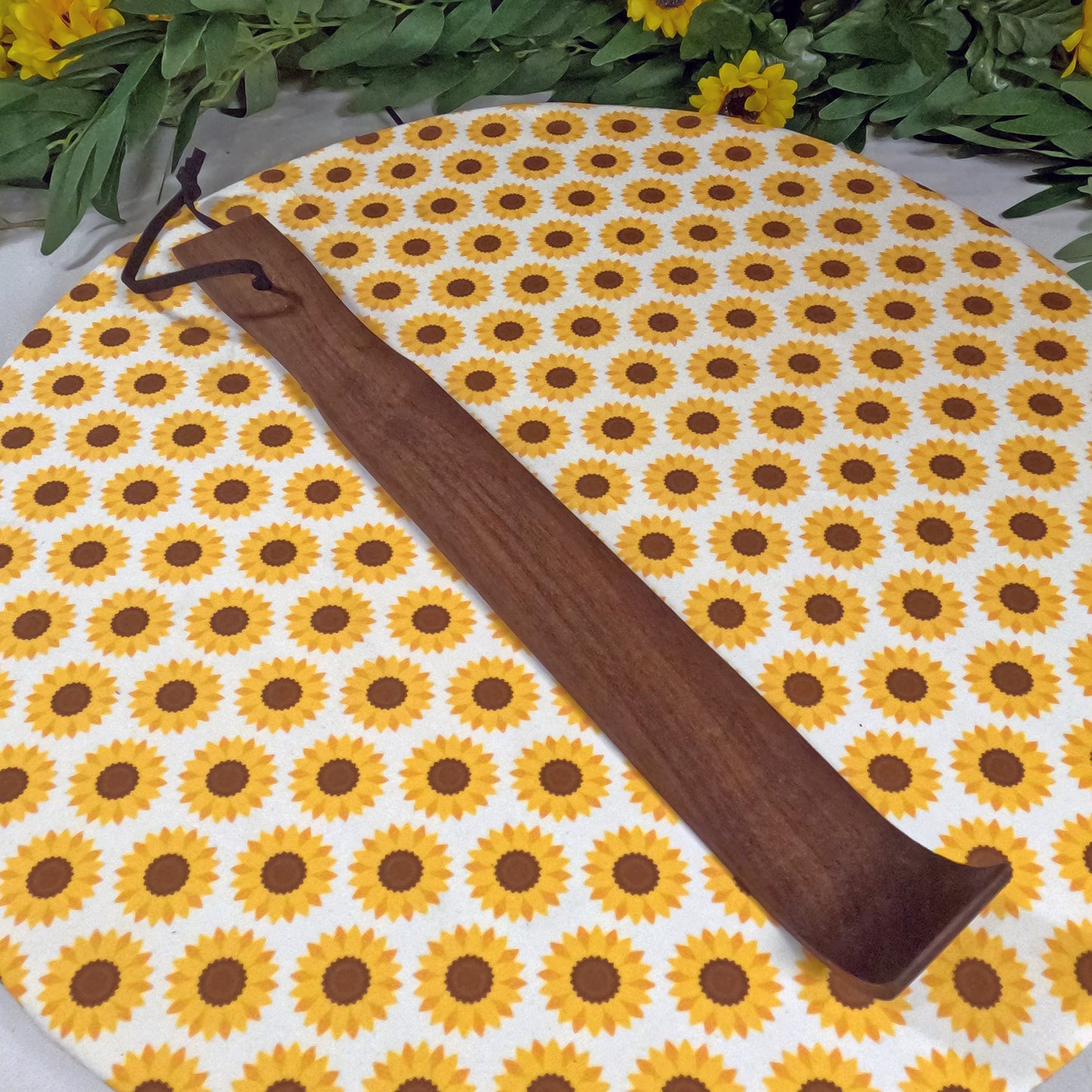 Wooden back scratcher  on a sunflower-patterned mat with greenery around