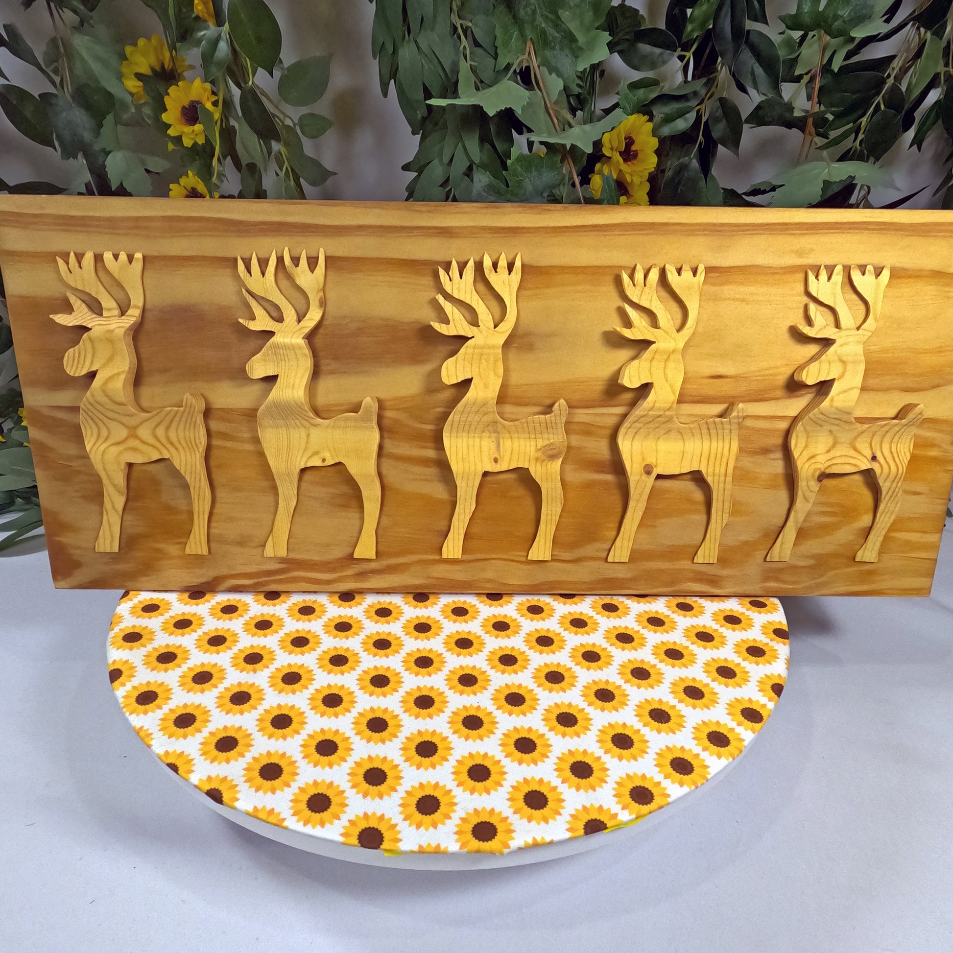 Wooden wall art with deer carvings and a sunflower-patterned plate below.
