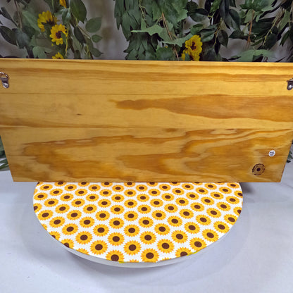 Wooden placque with a sunflower patterned base on a white surface.