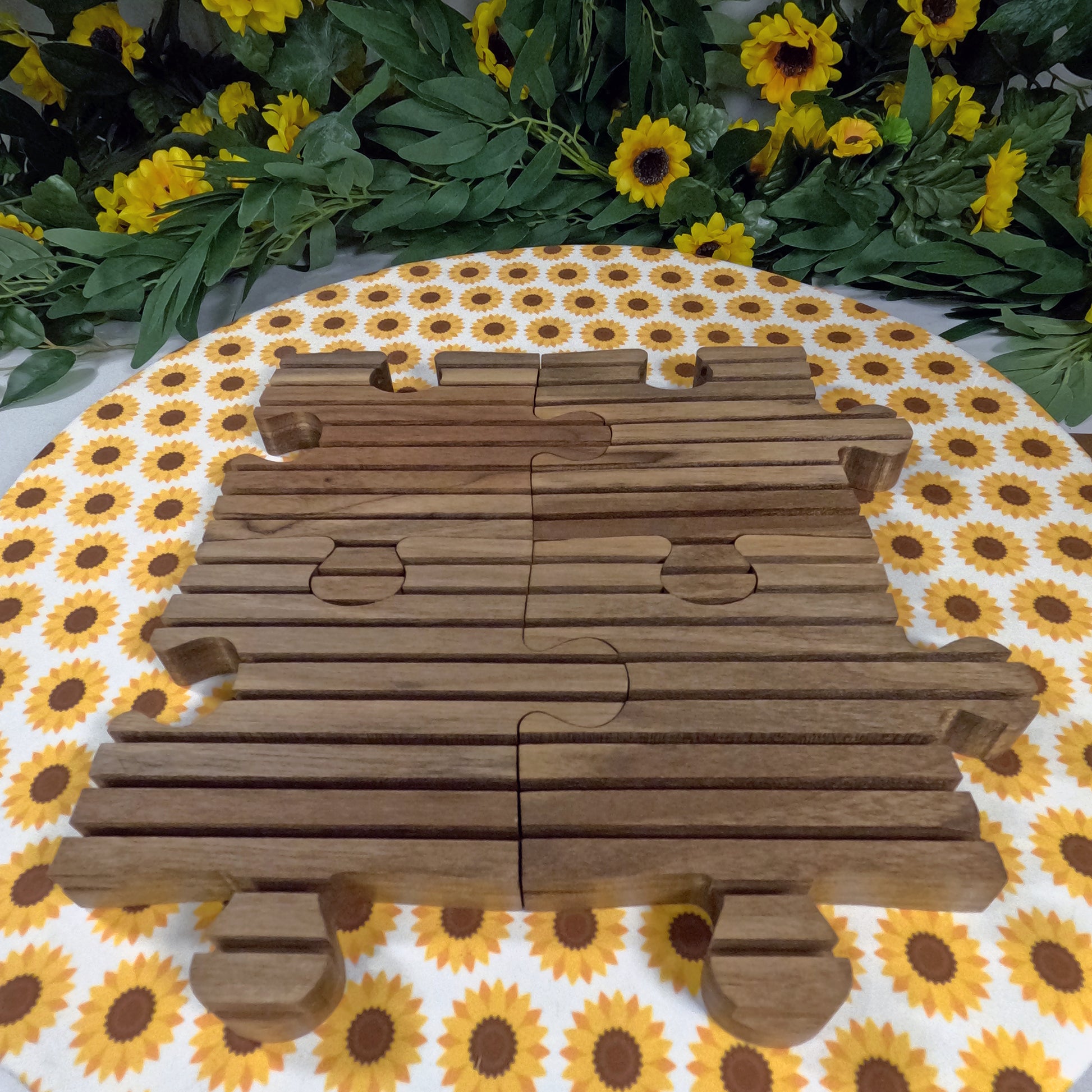 Wooden puzzle trivet train on a floral tablecloth with sunflowers and greenery.
