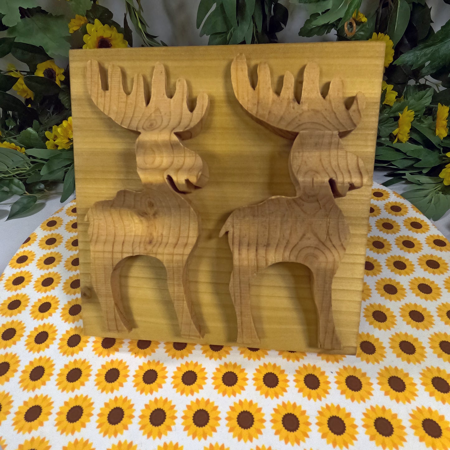 Wooden moose-shaped cutouts on a wooden board with a sunflower-patterned tablecloth.