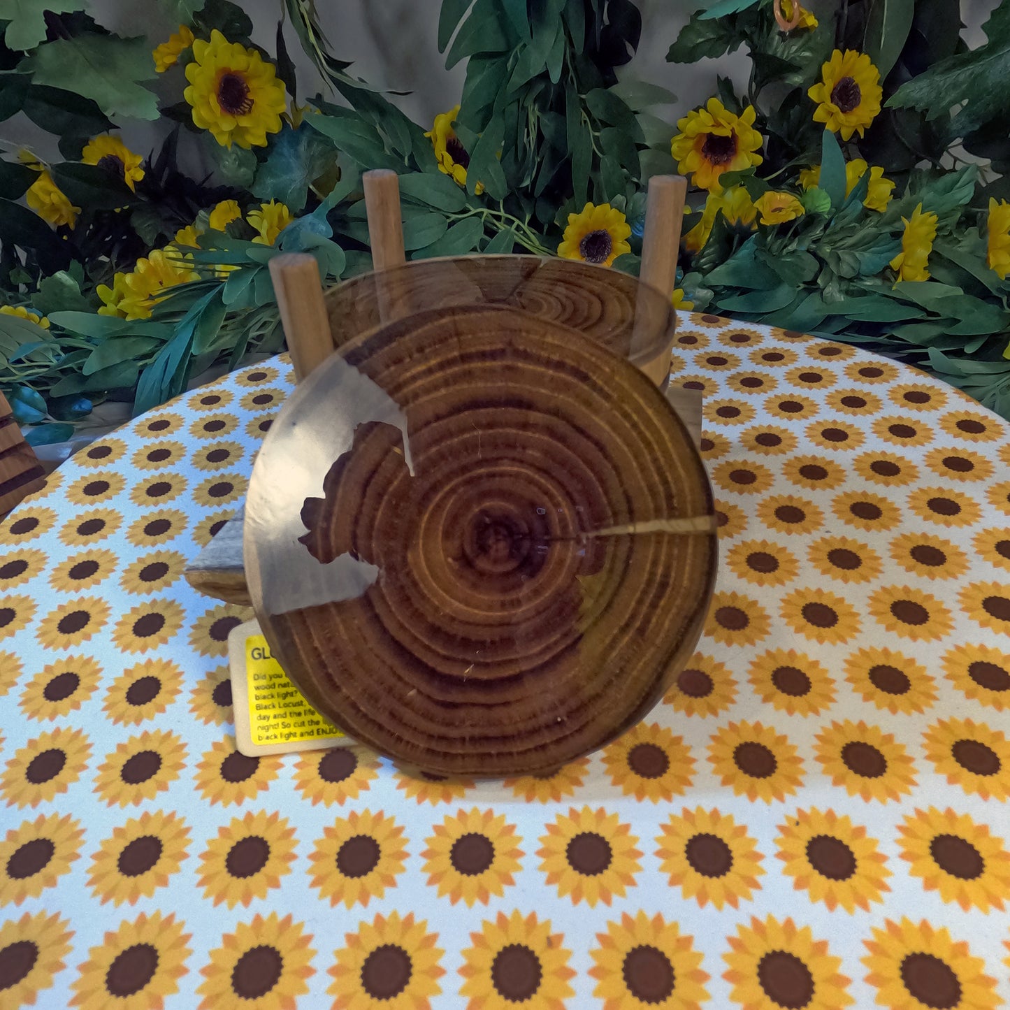 Wooden coasters on a tablecloth with sunflower pattern, surrounded by flowers and greenery