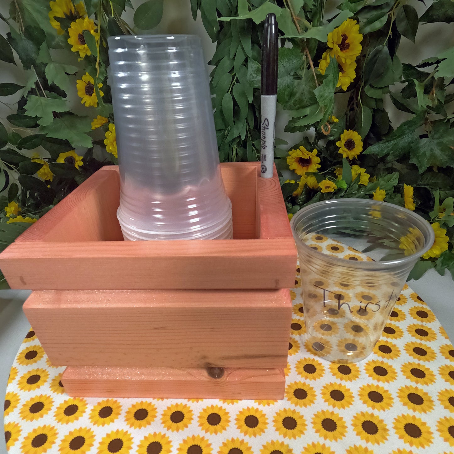 Stack of clear plastic cups in a wooden holder with a floral background