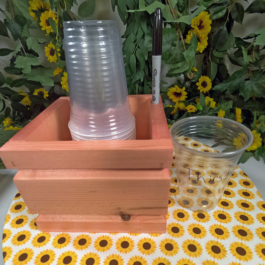 Stack of clear plastic cups in a wooden holder with a floral background