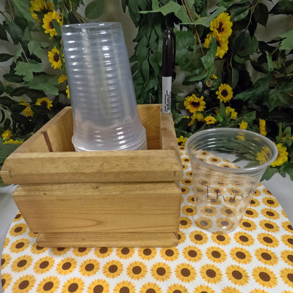 Wooden cup holder with clear plastic cups on a tablecloth with sunflower pattern