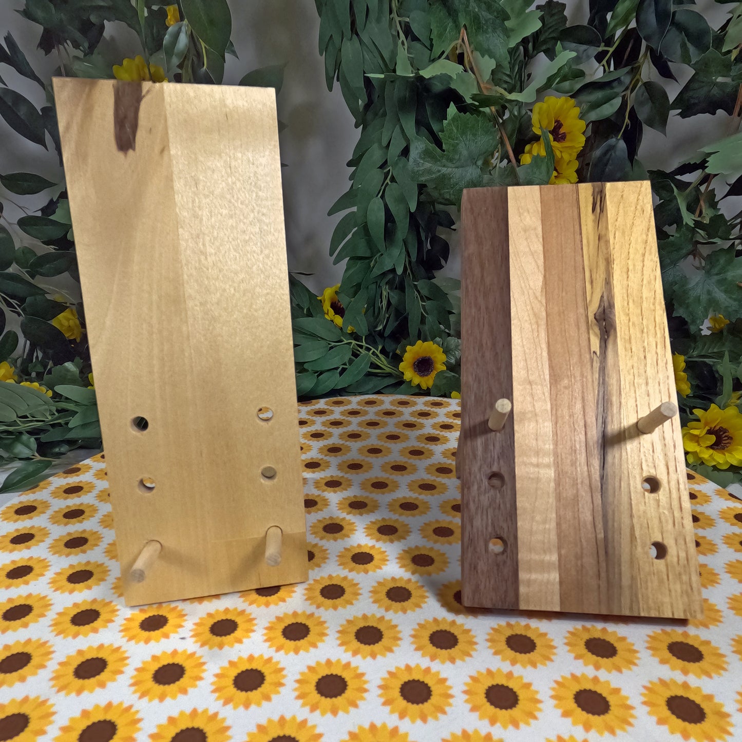 Two wooden cell phone stands with holes on a tablecloth with sunflower pattern