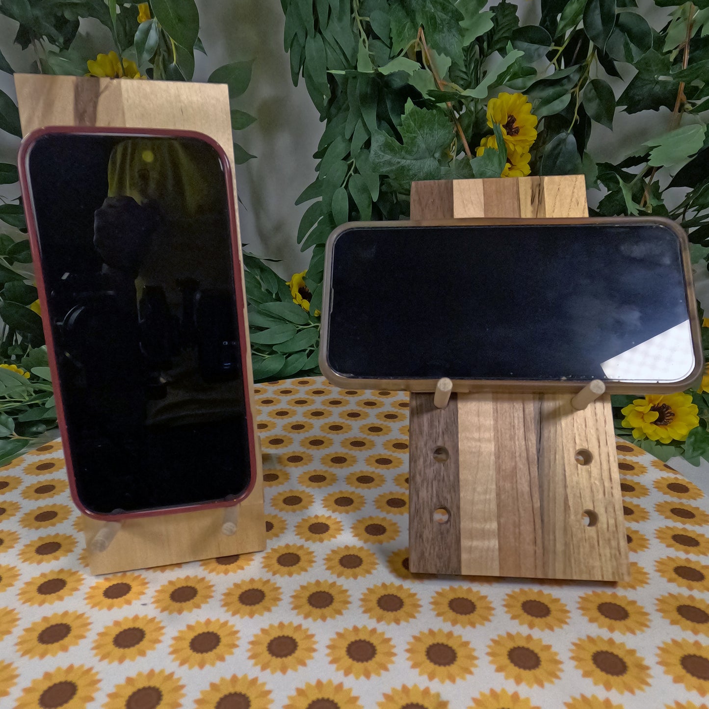 Two wooden phone stands on a table with a floral tablecloth and green plants in the background.