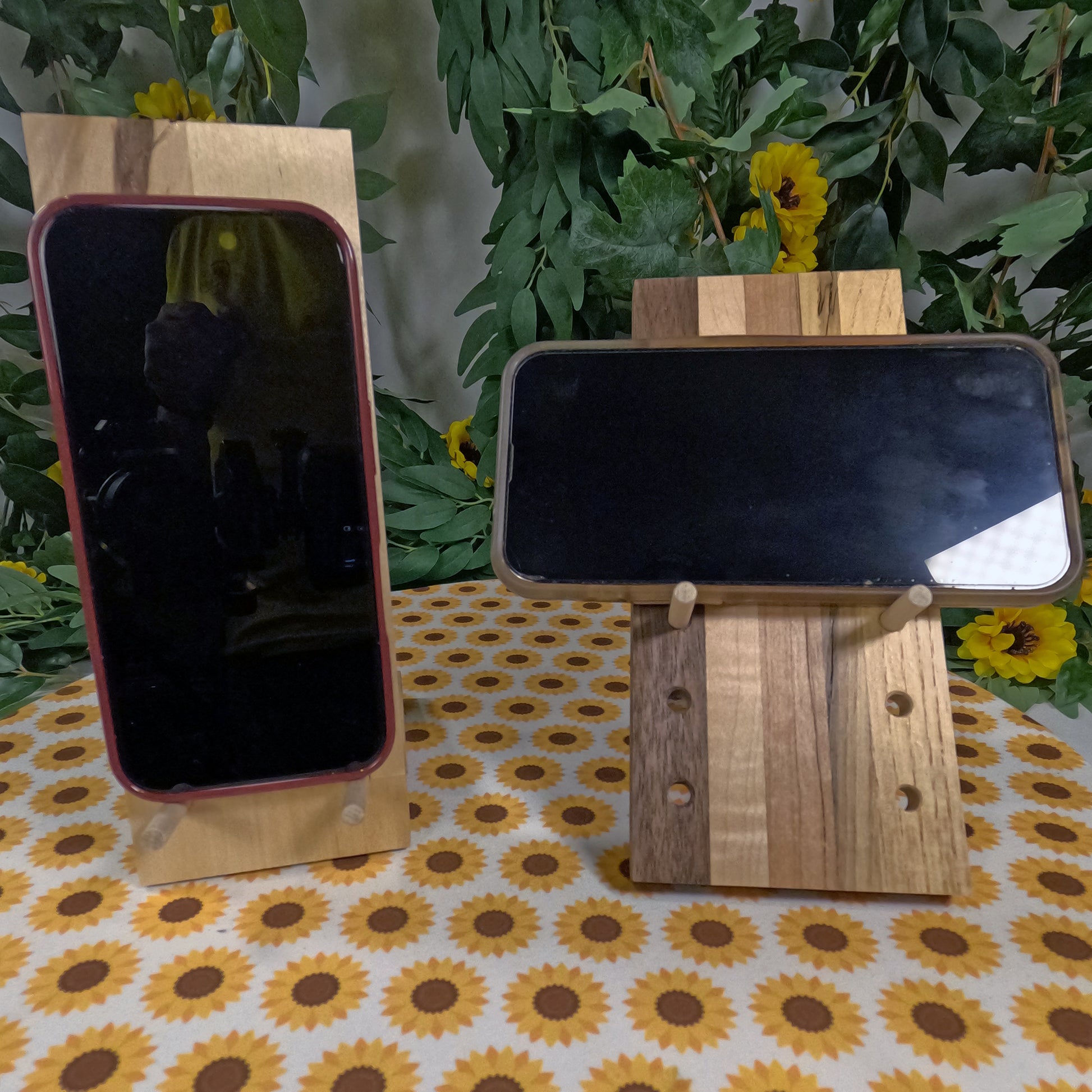 Two wooden phone stands on a table with a floral tablecloth and green plants in the background.
