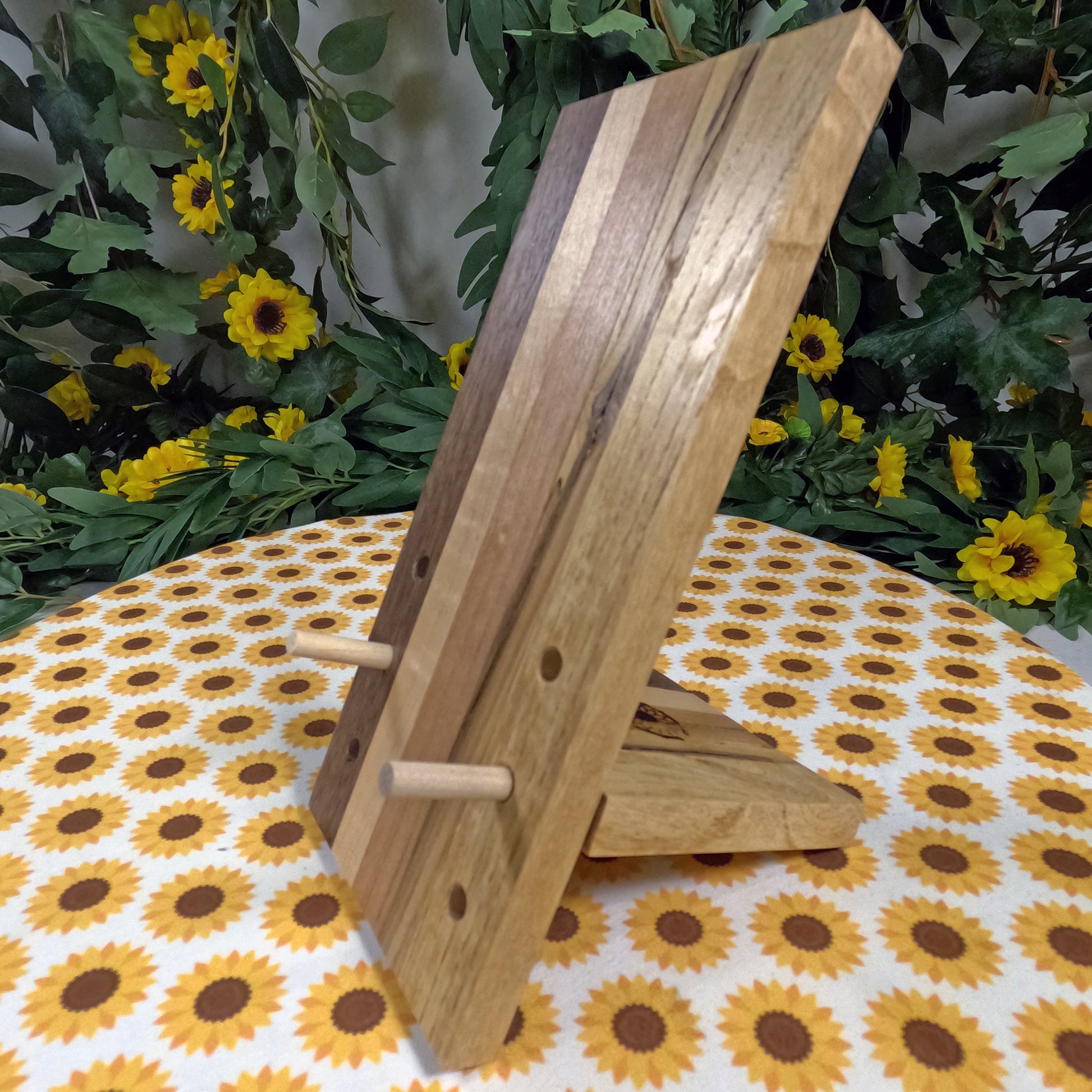 Wooden phone stand on a tablecloth with sunflower pattern, surrounded by greenery and flowers.