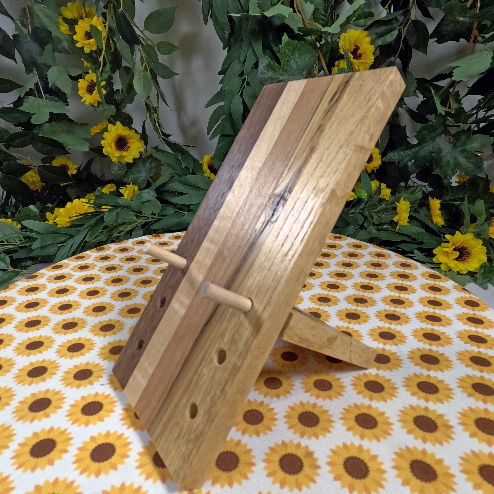 Wooden phone stand on a tablecloth with sunflower pattern, surrounded by greenery and flowers.