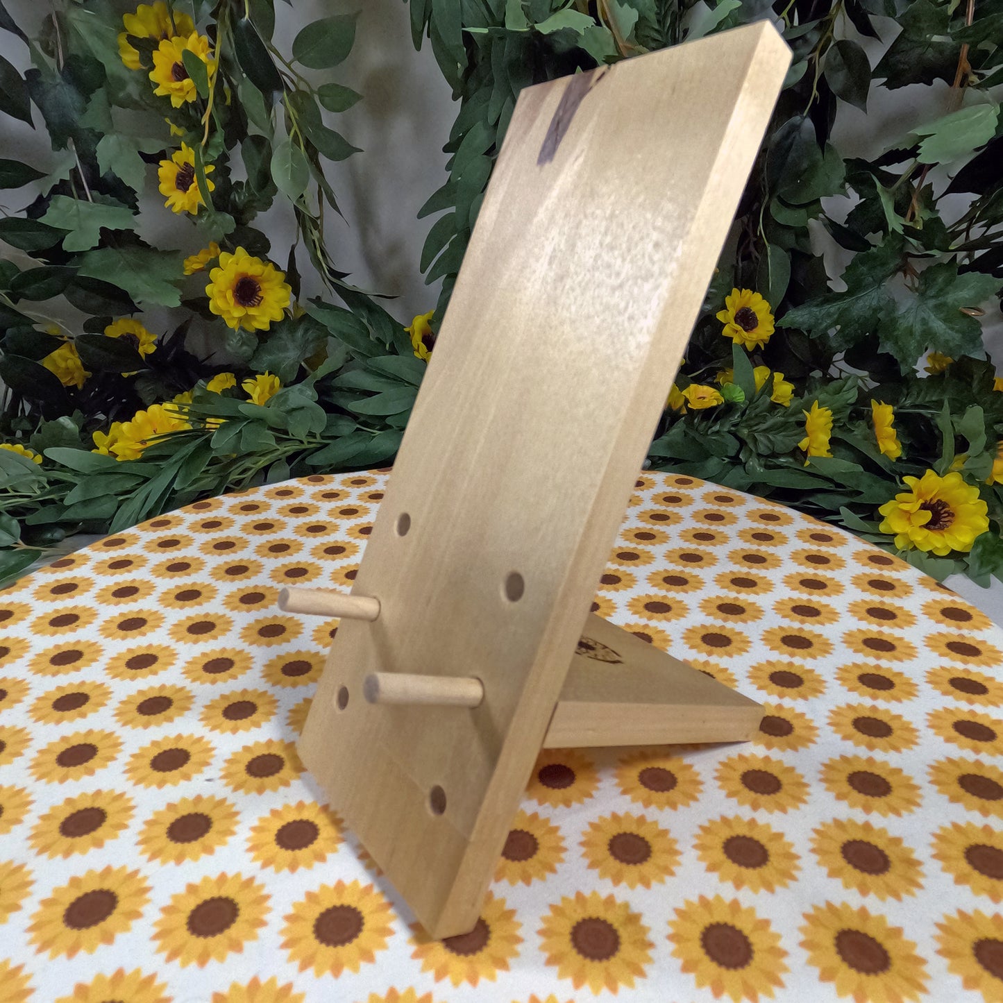 Wooden phone stand on a tablecloth with sunflower pattern, surrounded by greenery and flowers.