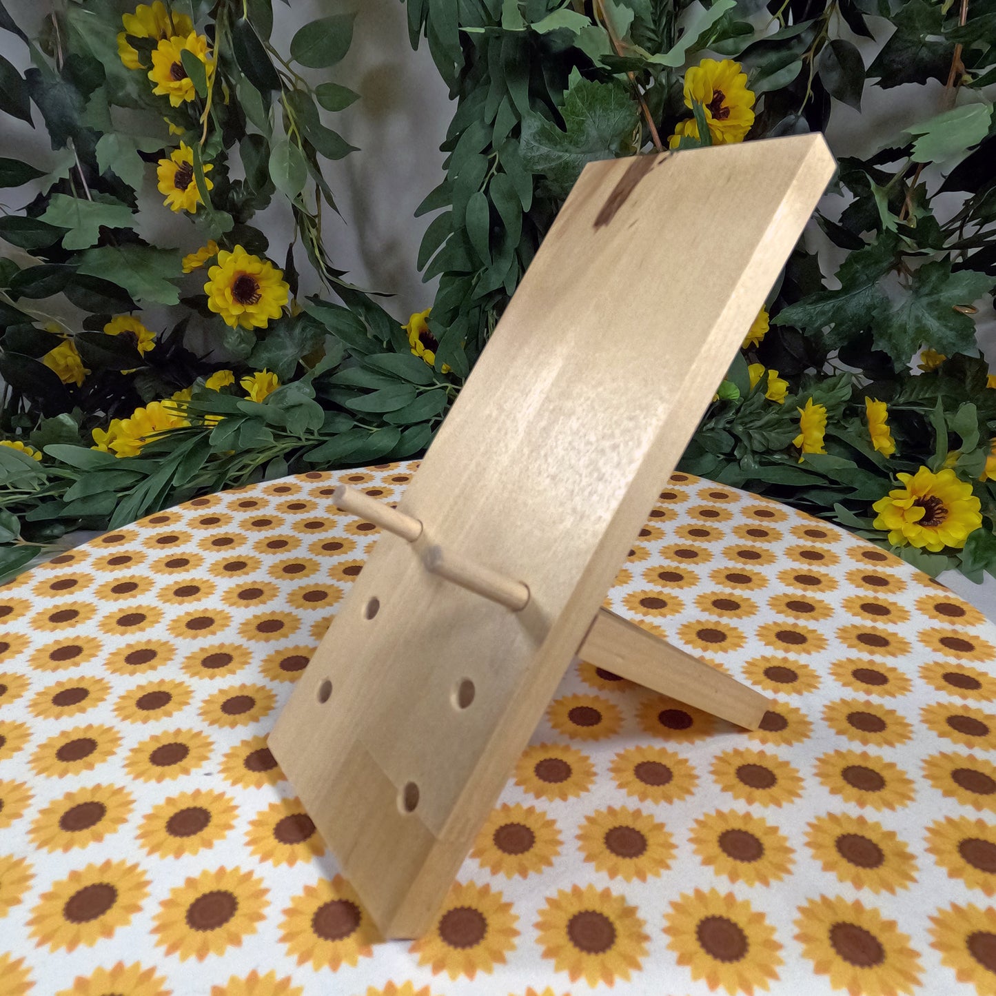 Wooden phone stand on a tablecloth with sunflower pattern, surrounded by greenery and flowers.