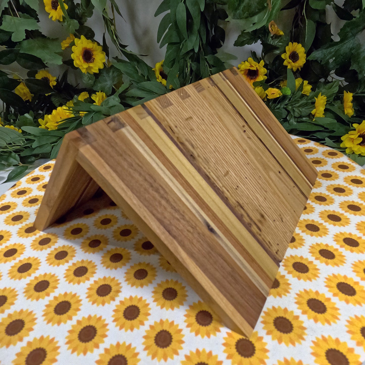 Wooden book stand on a tablecloth with sunflower pattern, surrounded by greenery and yellow flowers.