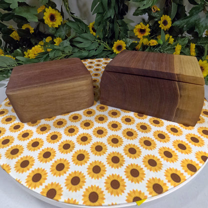 Two wooden boxes on a tablecloth with sunflower pattern, surrounded by greenery and sunflowers.