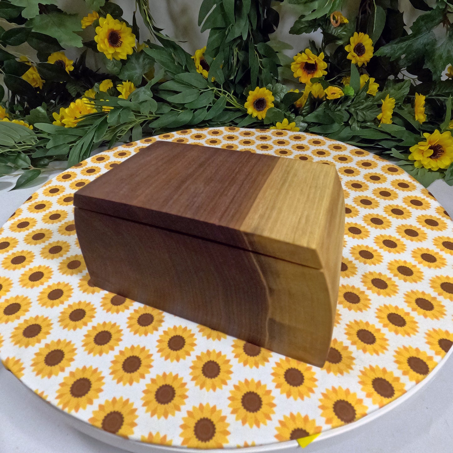 Wooden box on a sunflower-patterned surface with greenery and flowers in the background