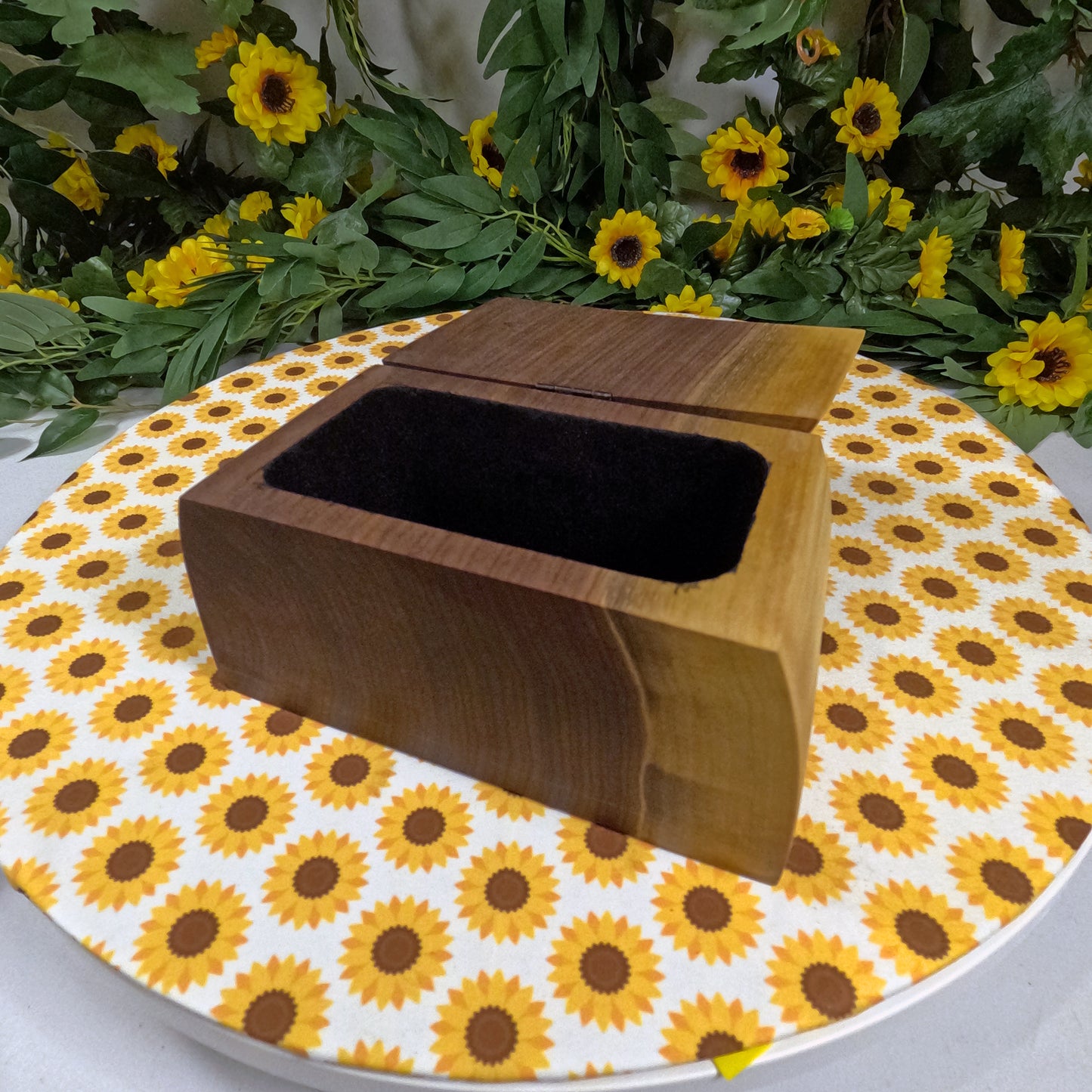 Wooden box on a tablecloth with sunflower pattern, surrounded by flowers.