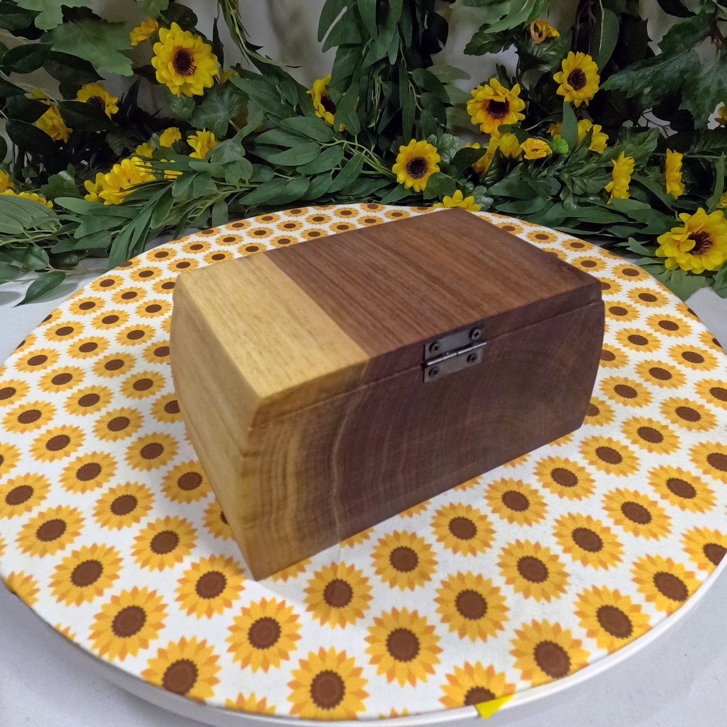 Wooden box on a tablecloth with sunflower pattern, surrounded by greenery and yellow flowers.