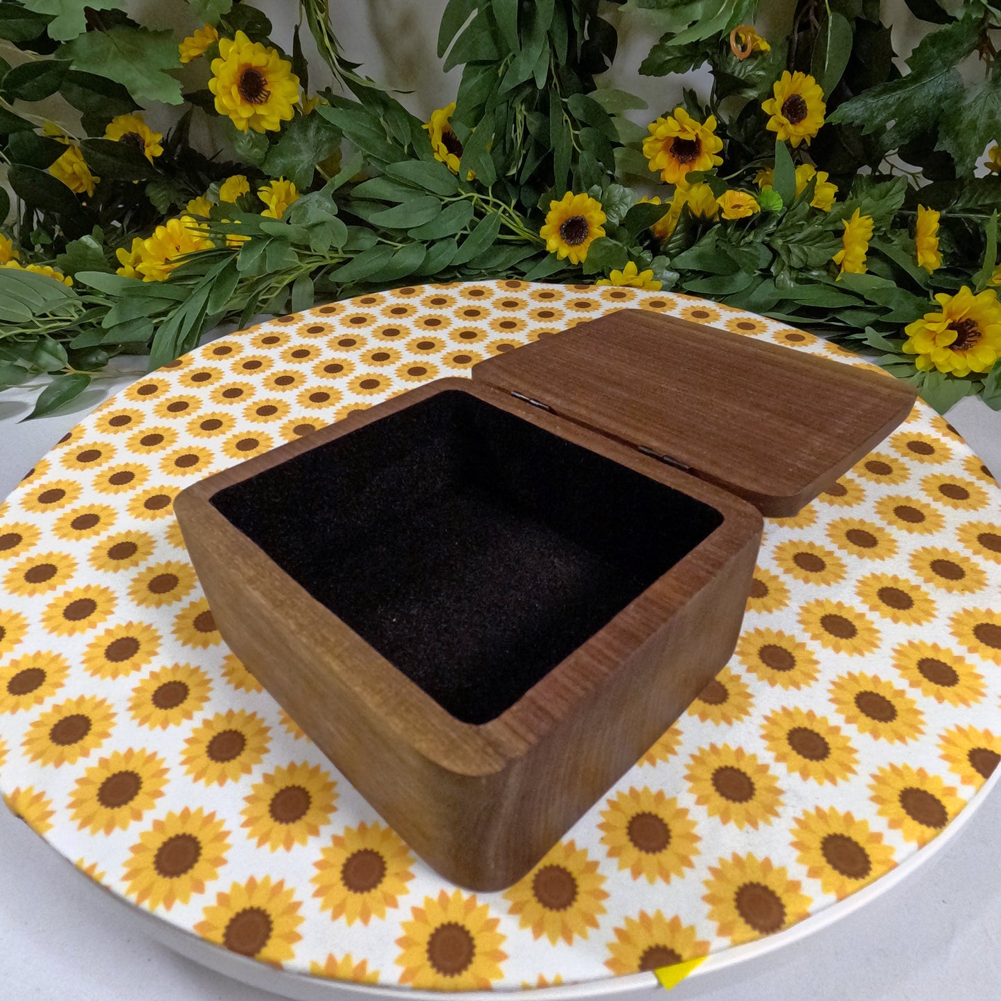 Wooden box on a sunflower-patterned surface with greenery and flowers in the background