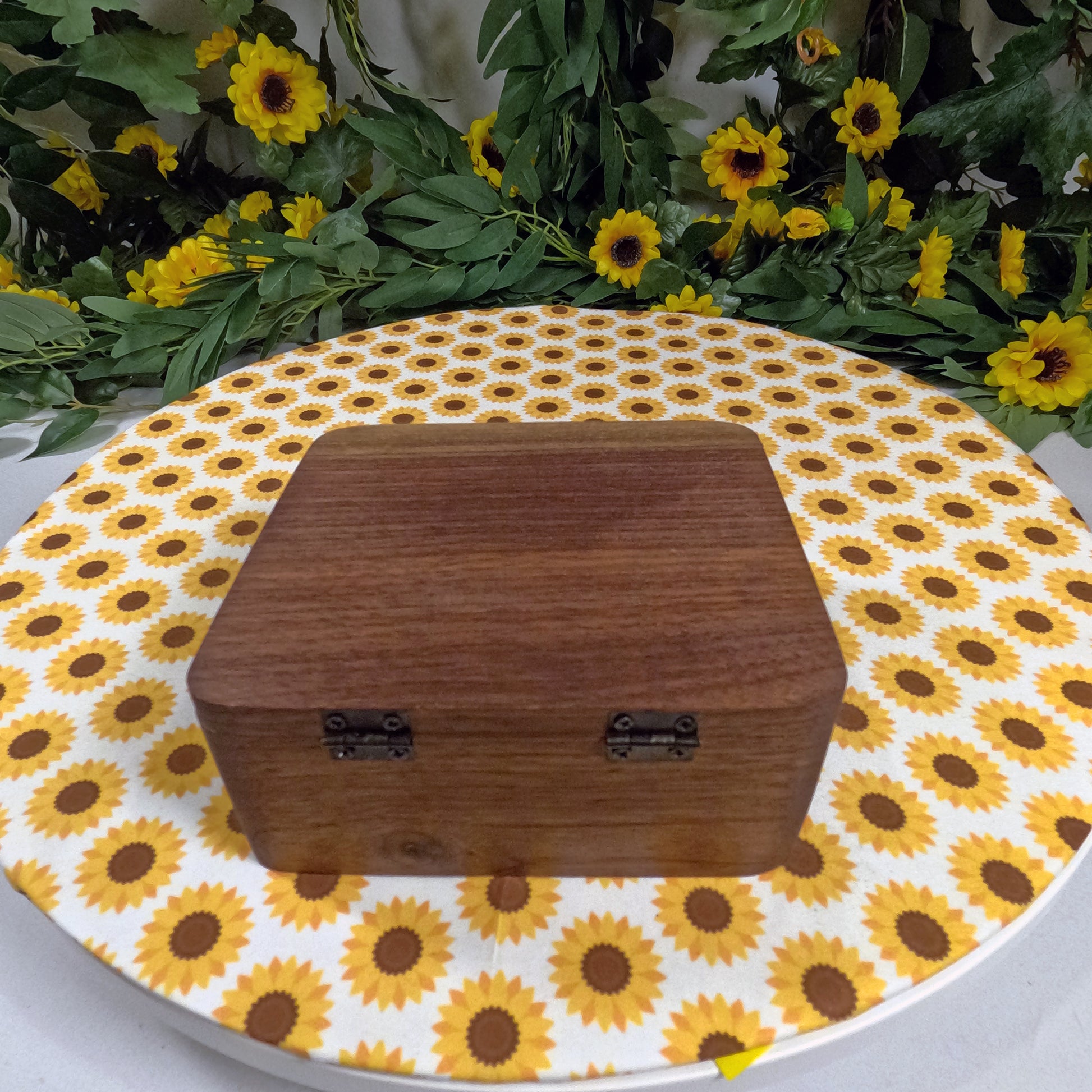 Wooden box on a sunflower-patterned surface with greenery in the background