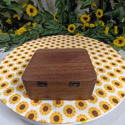 Wooden box on a sunflower-patterned surface with greenery in the background
