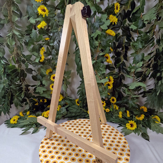 Wooden easel on a polka dot stool with greenery and yellow flowers in the background