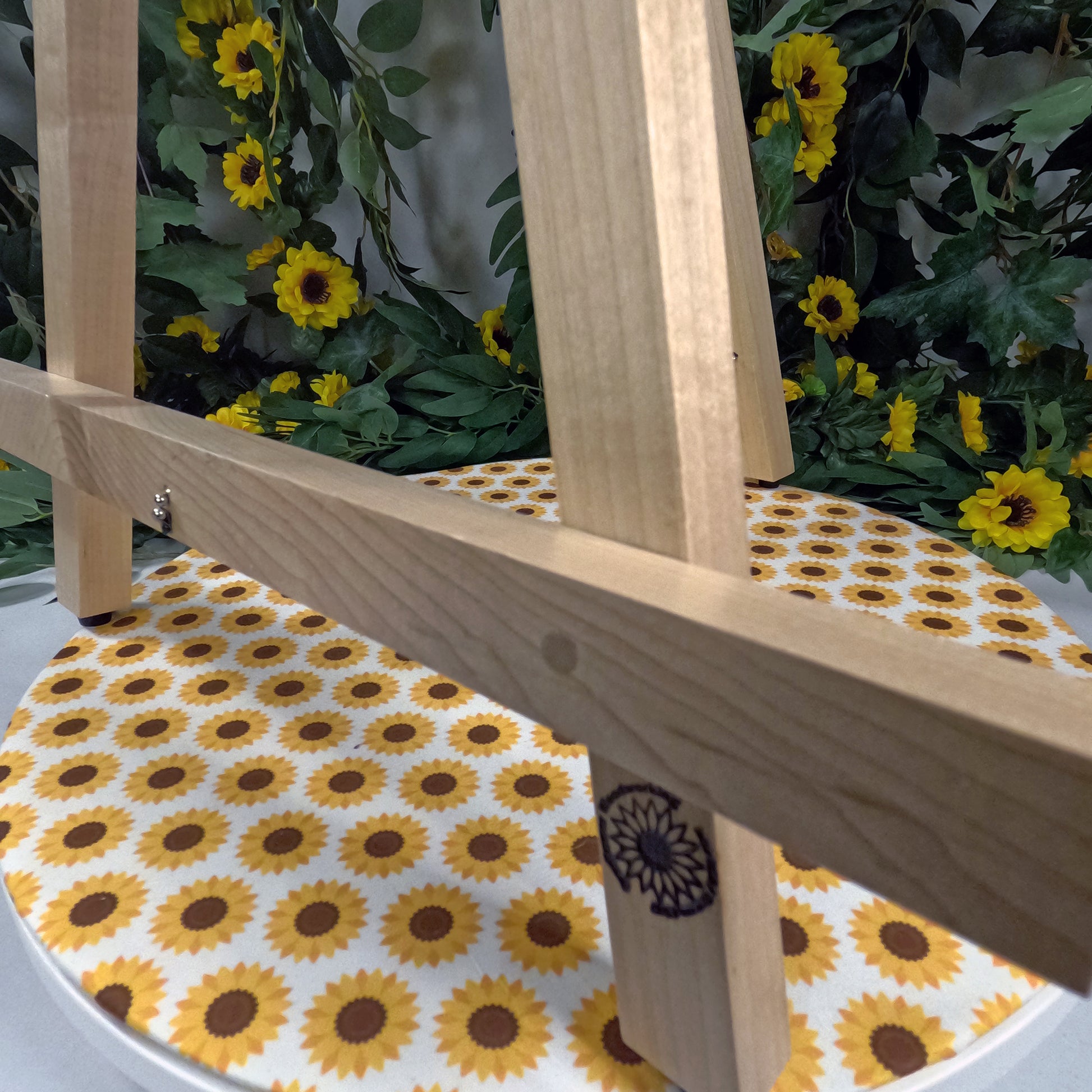 Wooden easel with a sunflower patterned clothe, against a background of sunflowers and greenery.