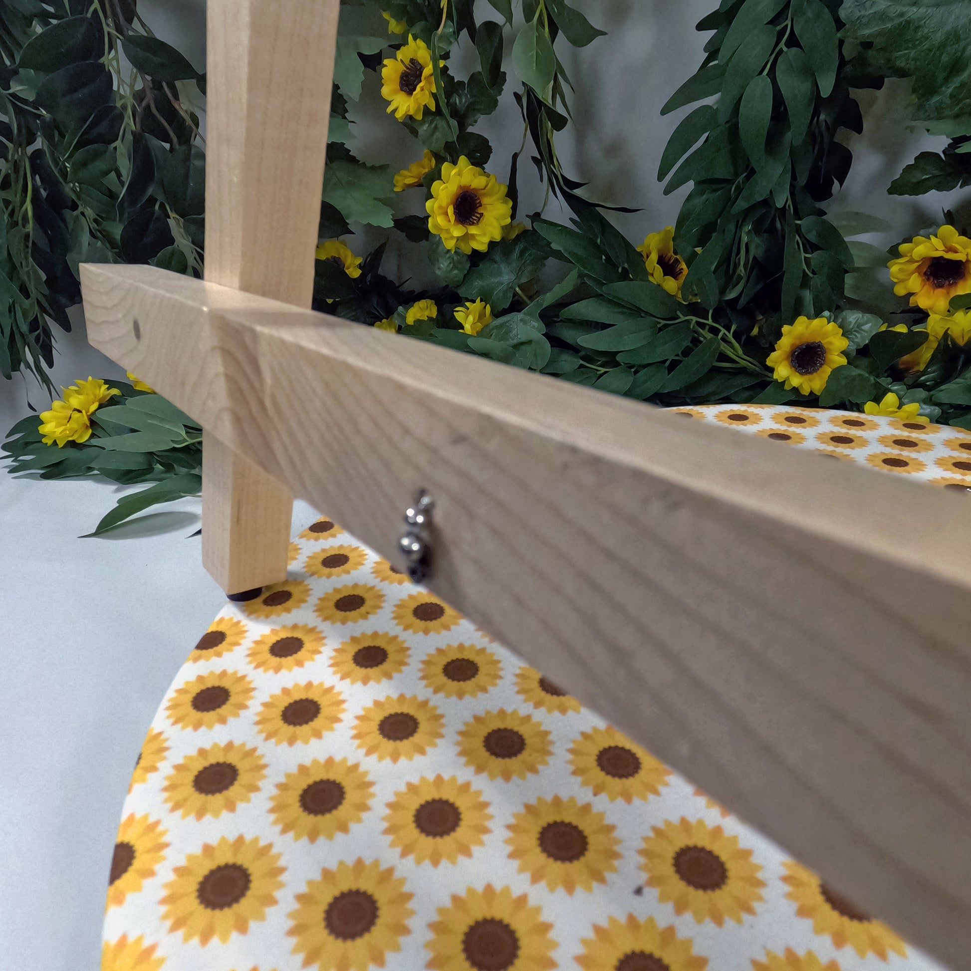 Wooden easel with a sunflower patterned tablecloth against a backdrop of greenery and sunflowers.